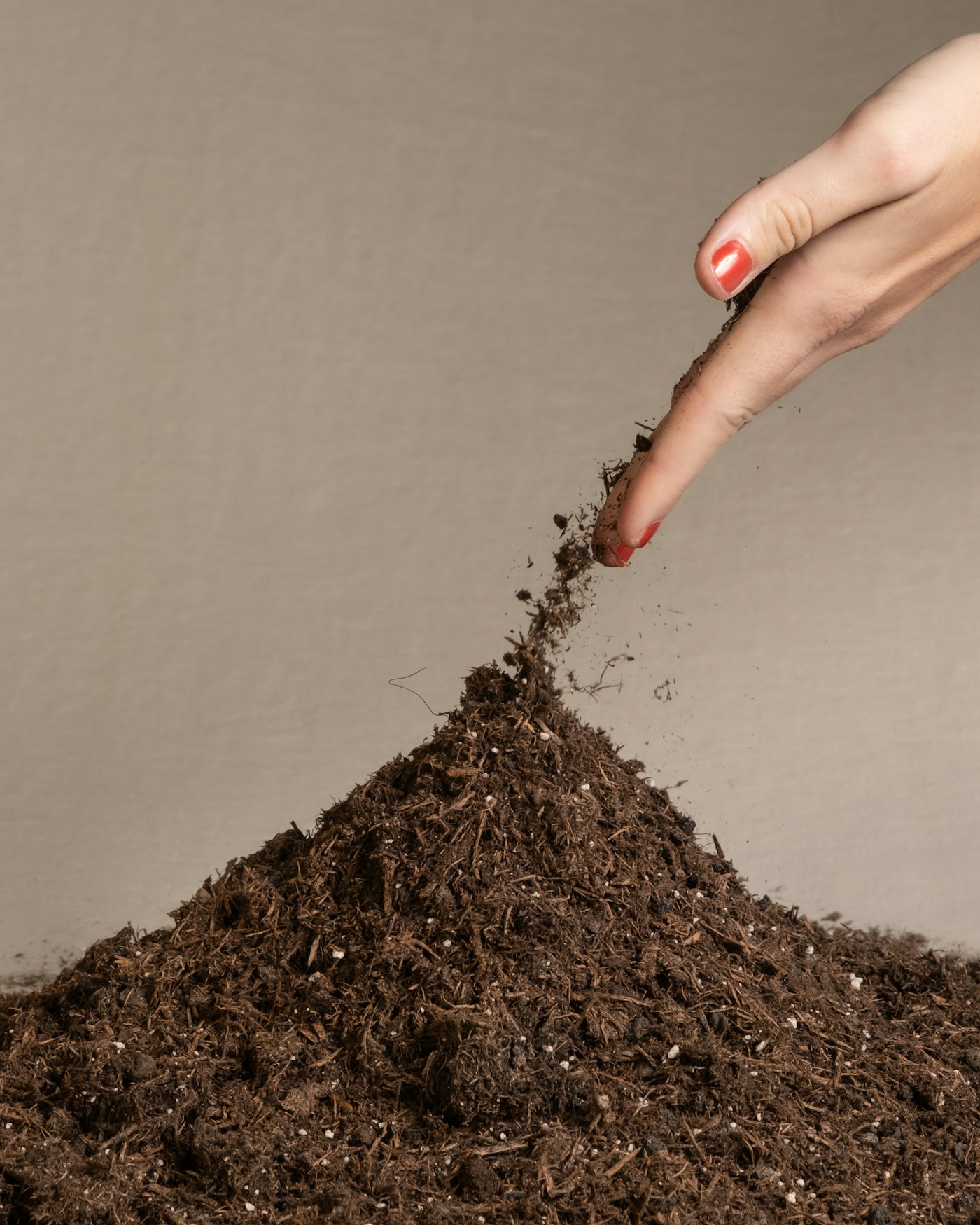 A hand sprinkling dark, crumbly compost onto a pile