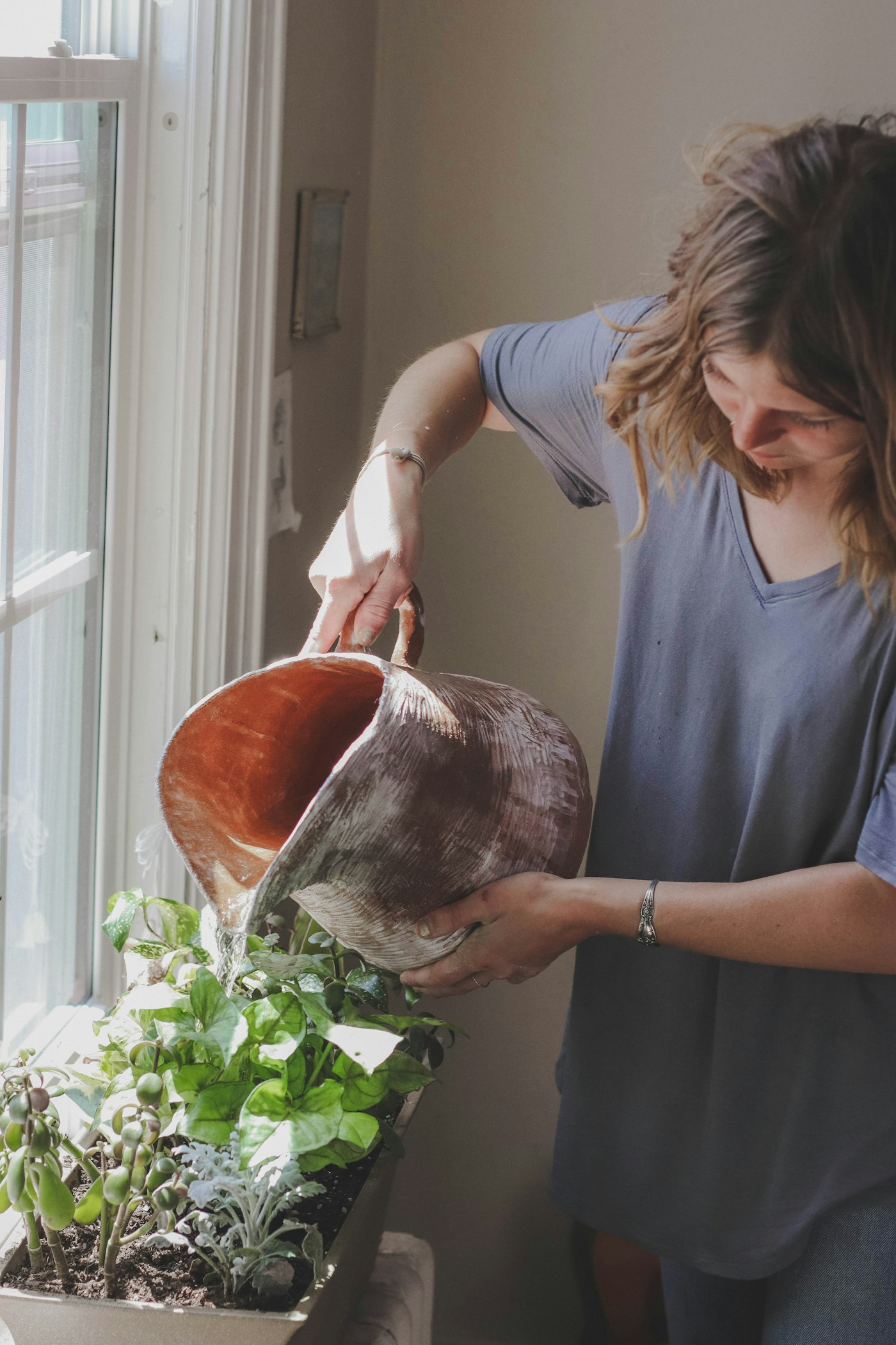 A woman watering a potted plant on a sunny windowsill